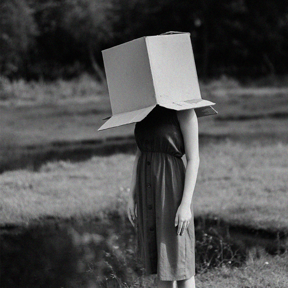 Faceless Women barefeet on a field with box on top of her head hiding her face